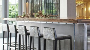 Un espace bar moderne avec un comptoir en marbre, des chaises en métal et une vue sur la verdure environnante.