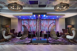 A modern lobby with a central seating area, a decorative tree, and ambient lighting.