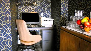 A small office with a desk, chair, computer, printer, and a fruit bowl on the counter.