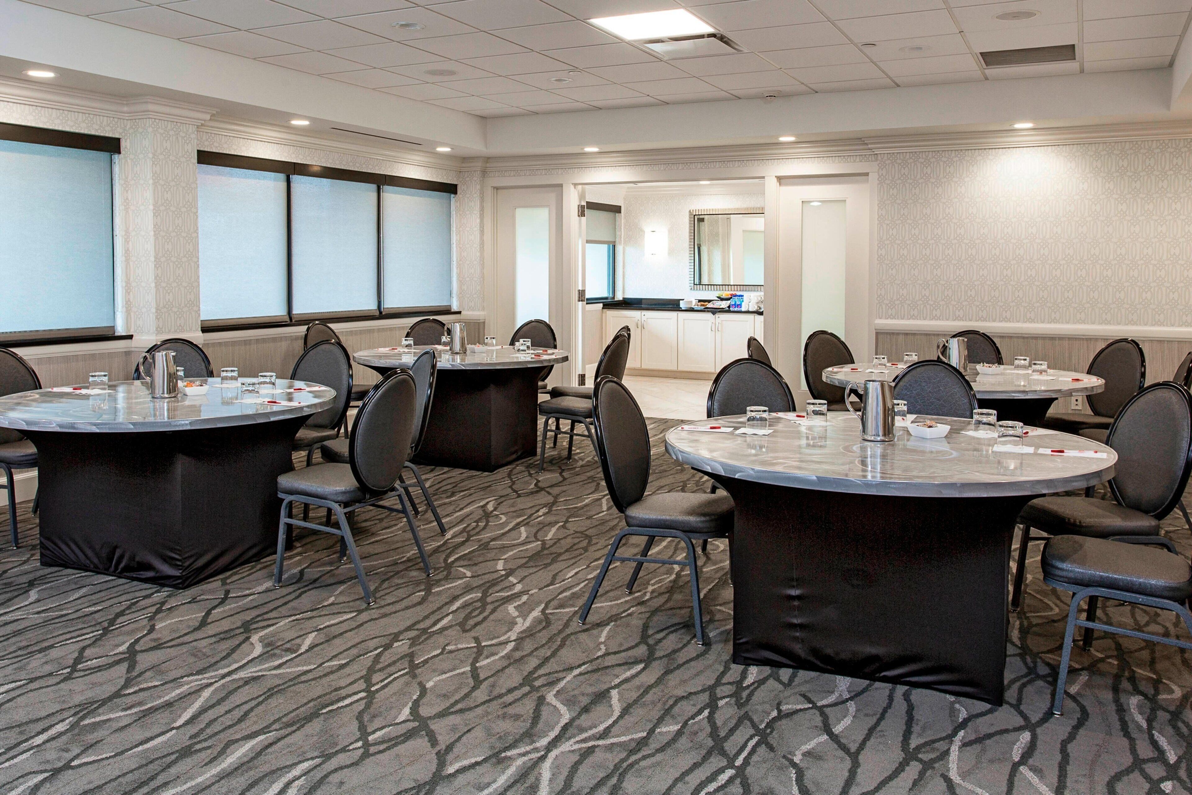 A conference room with multiple round tables, chairs, and a kitchenette area.