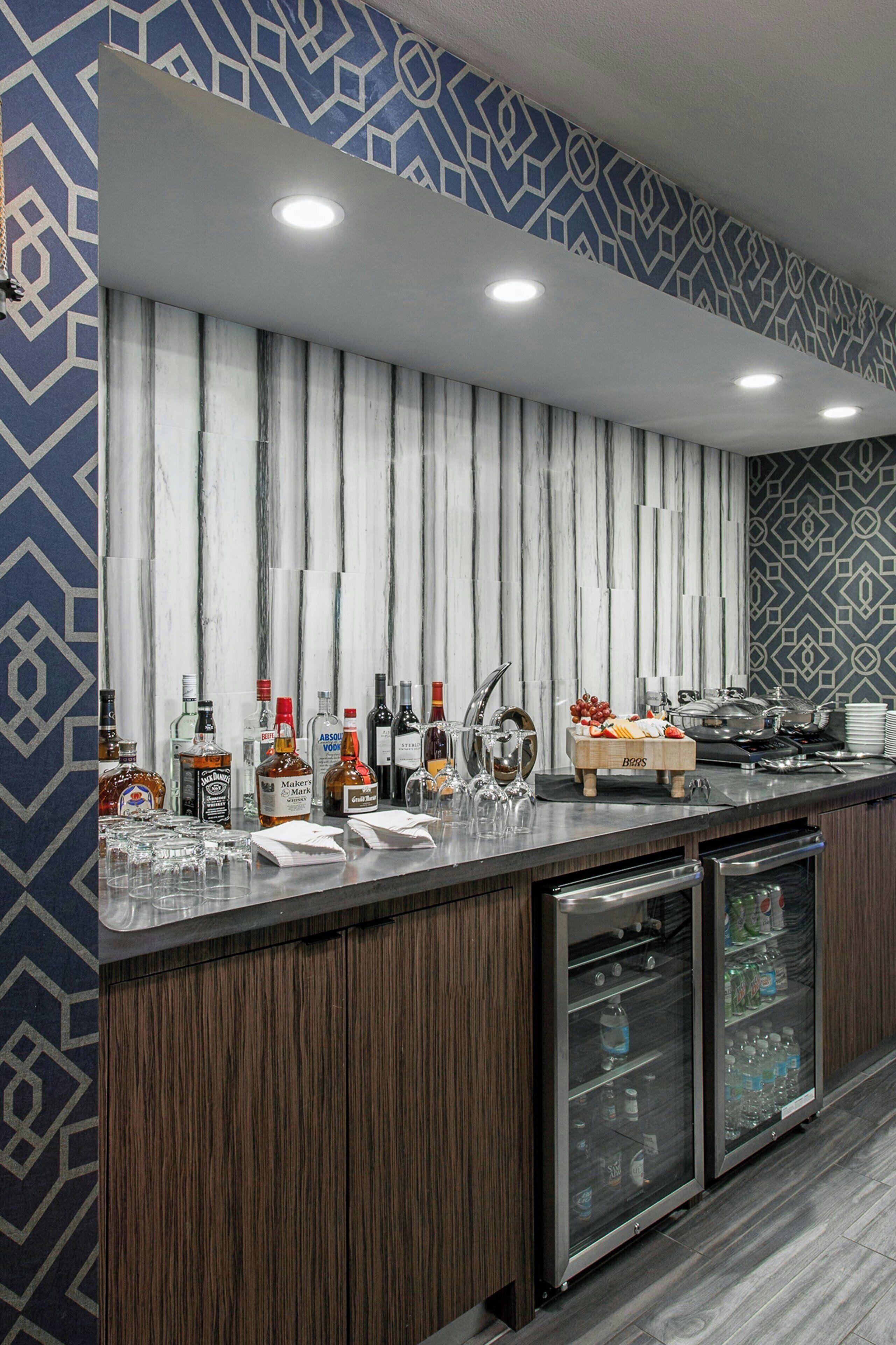 Eine moderne Bar mit einer Marmorplatte, verschiedenen Spirituosenflaschen, Gläsern und einer Obstschale.