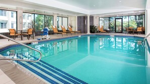 Une piscine intérieure à l’eau d’un bleu limpide, entourée de chaises longues et de tables.