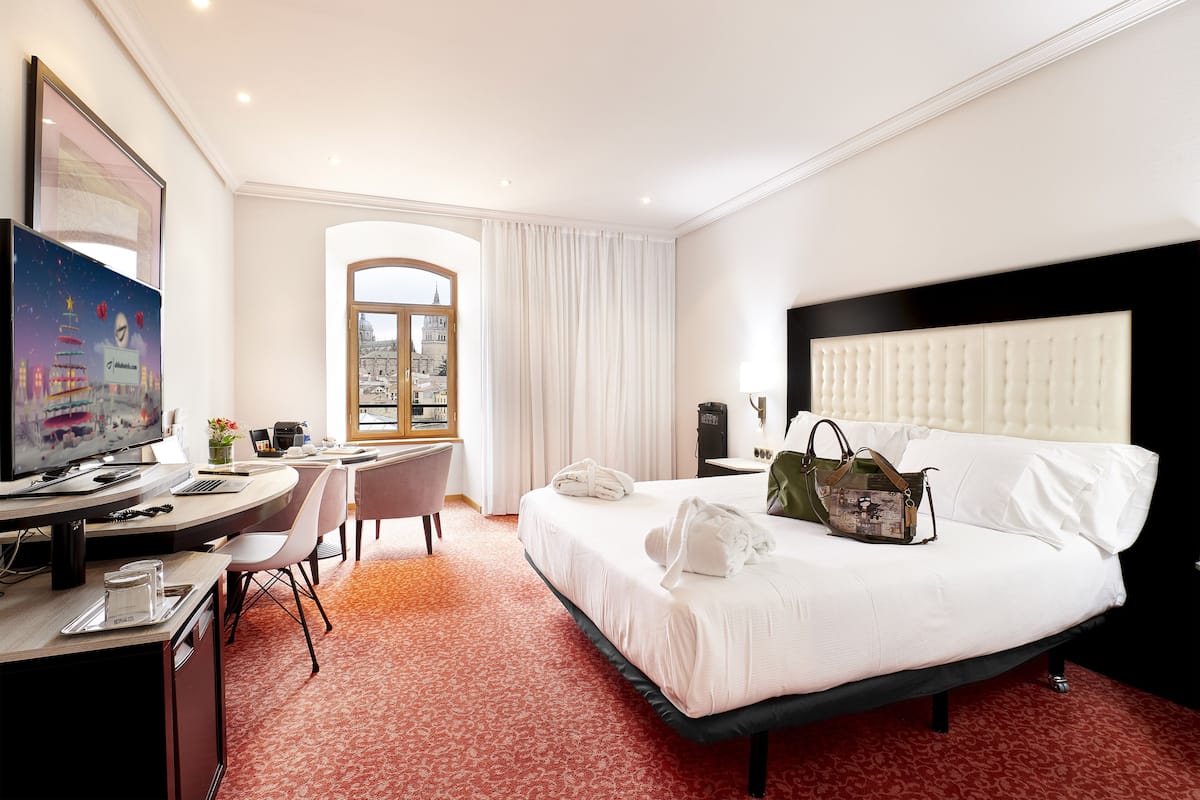 Une chambre d’hôtel avec un lit, un bureau équipé d’un ordinateur, une chaise et une fenêtre donnant sur la ville.
