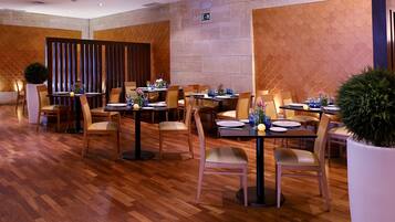 Un restaurante con suelo de madera, varias mesas dispuestas con sillas y plantas en macetas.