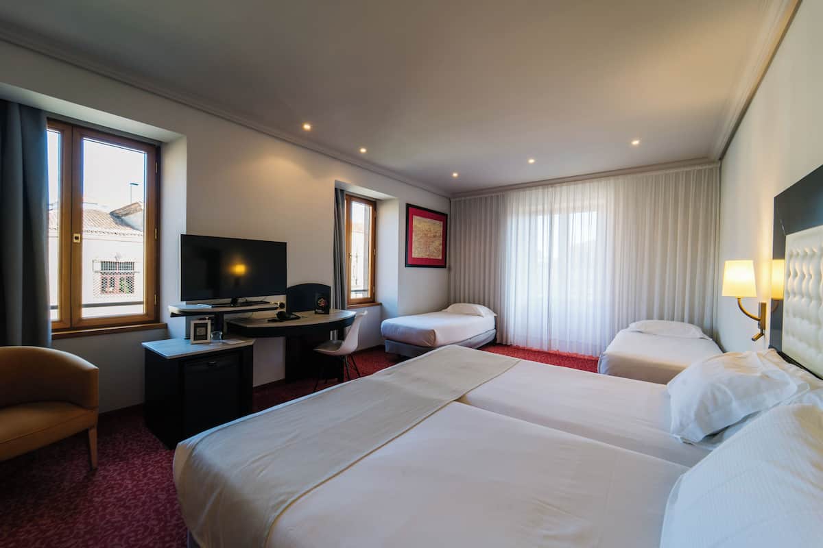 Une chambre d’hôtel avec deux lits, un bureau, une chaise, une télévision et une fenêtre avec des rideaux.