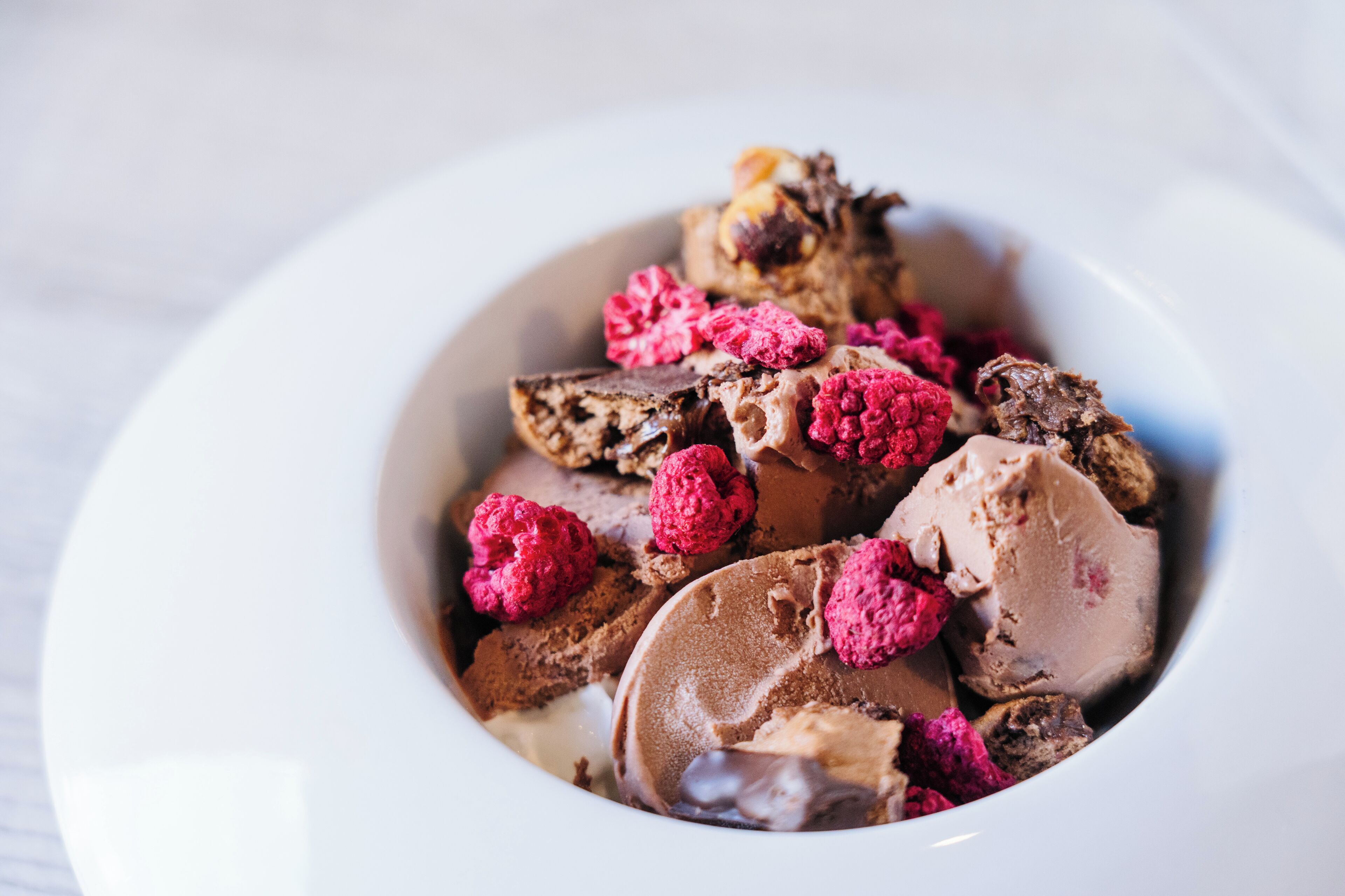 A bowl of chocolate ice cream with raspberries.