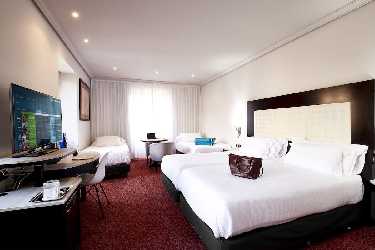 Une chambre d’hôtel avec deux lits, un bureau avec un ordinateur, une télévision et une grande fenêtre avec des rideaux.