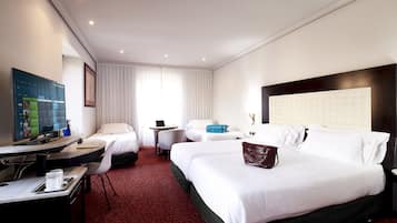 A hotel room with two beds, a desk with a computer, a TV, and a large window with curtains.