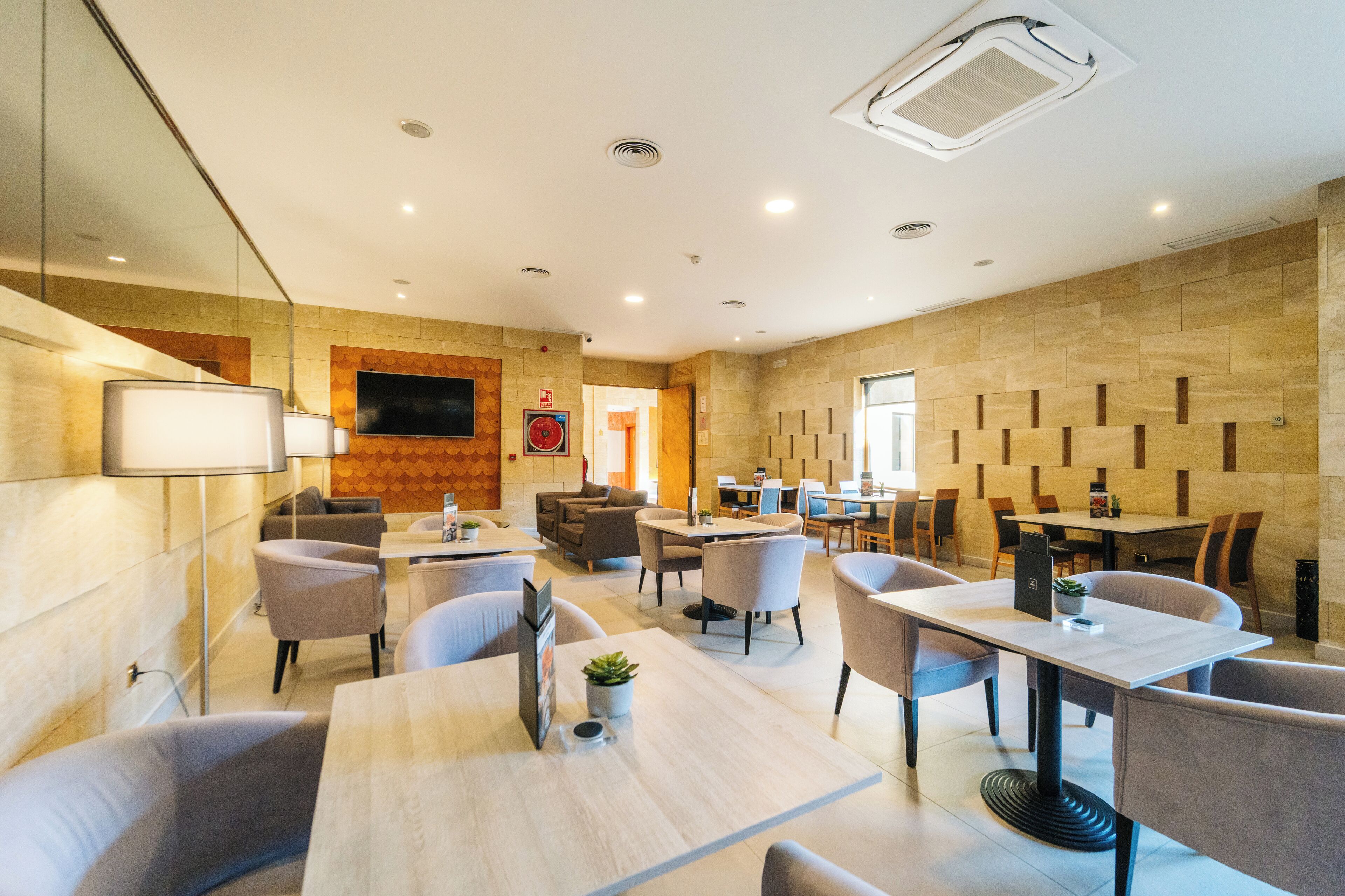 A modern hotel lobby with a mix of seating areas, including sofas and tables, and a large flat-screen TV mounted on the wall.