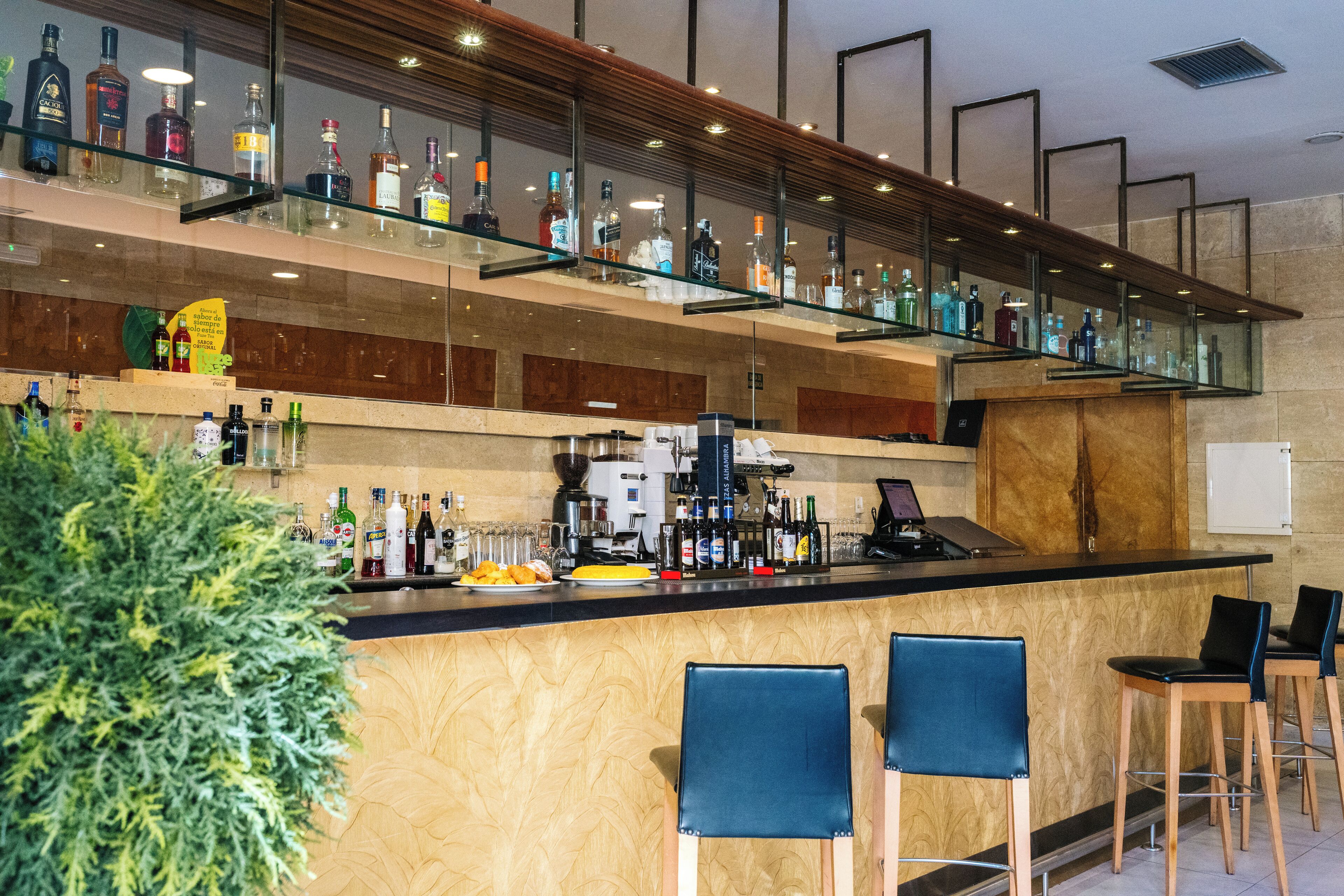 Un espace bar doté de plusieurs étagères remplies de bouteilles, d’une machine à café et de tabourets de bar.