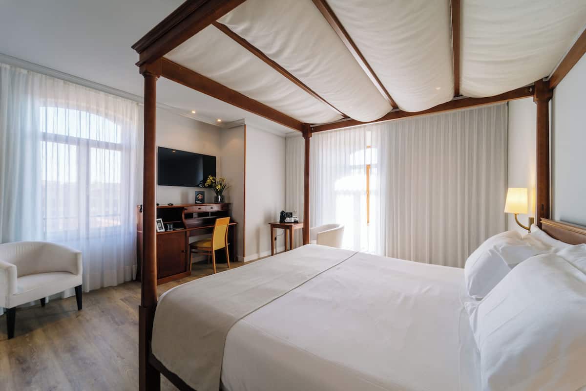 Une chambre d’hôtel avec un lit à baldaquin, un bureau avec une chaise, une télévision et une lampe.