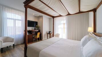 Habitación de hotel con cama con dosel, escritorio con silla, televisor y lámpara.