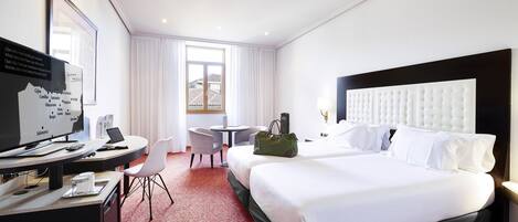 A hotel room with a large bed, a desk with a computer, a chair, and a small table.