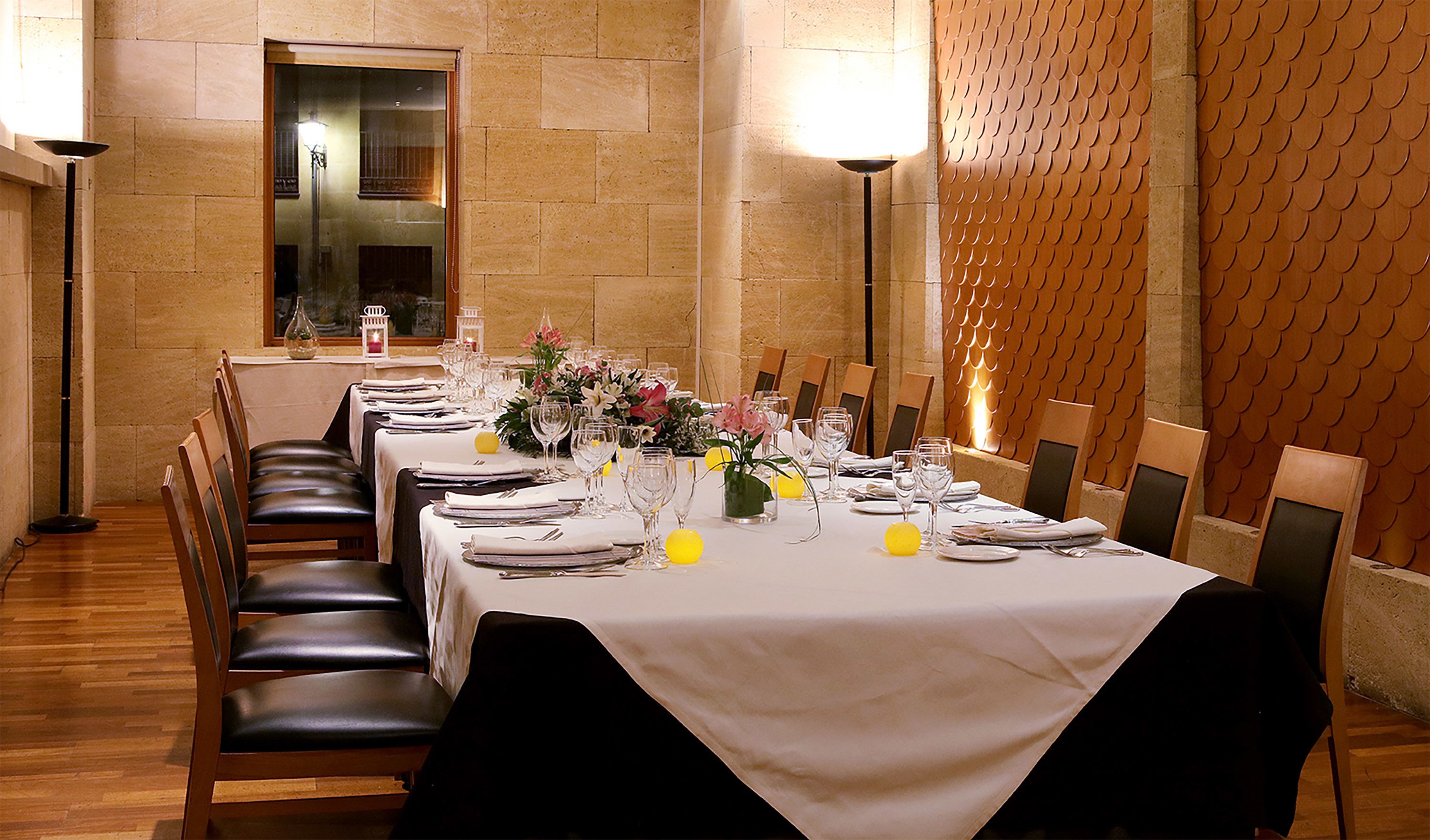 A long dining table set for a meal with chairs on both sides, a vase of flowers, and a candle on the table.