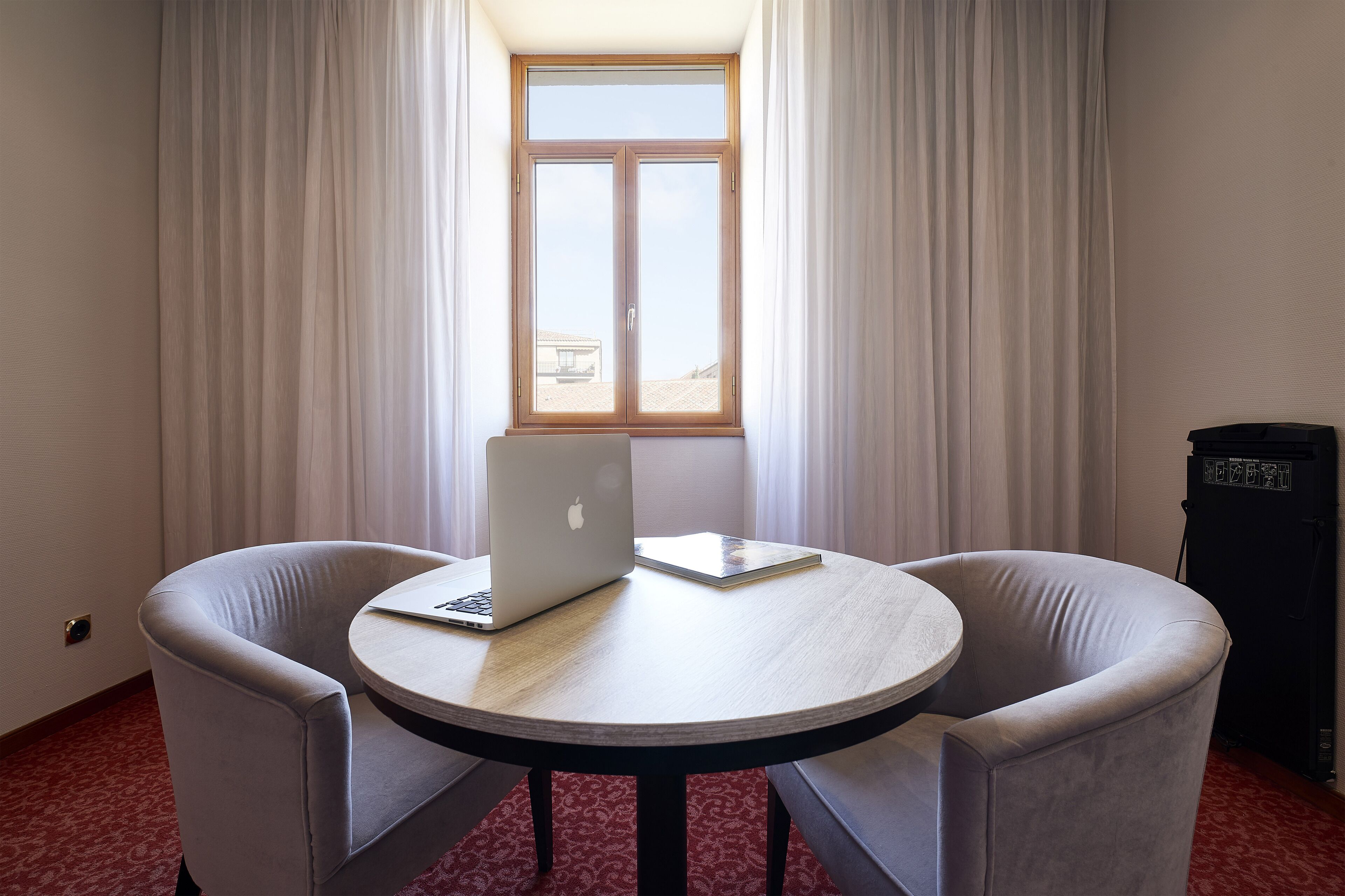A room with a round table, two armchairs, a laptop, and a window with curtains.