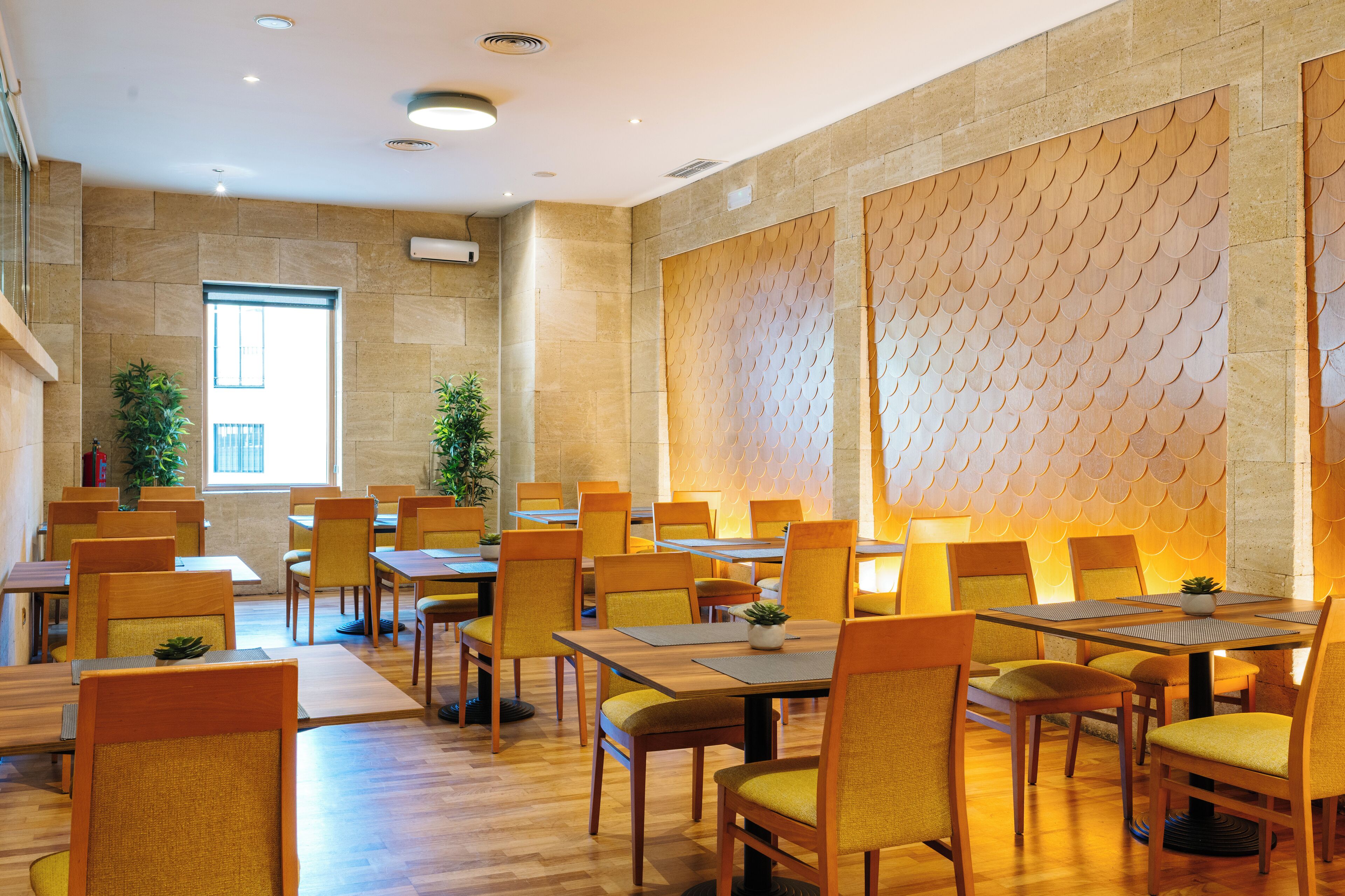 A spacious dining area with multiple tables and chairs, a large window, and a decorative wall.