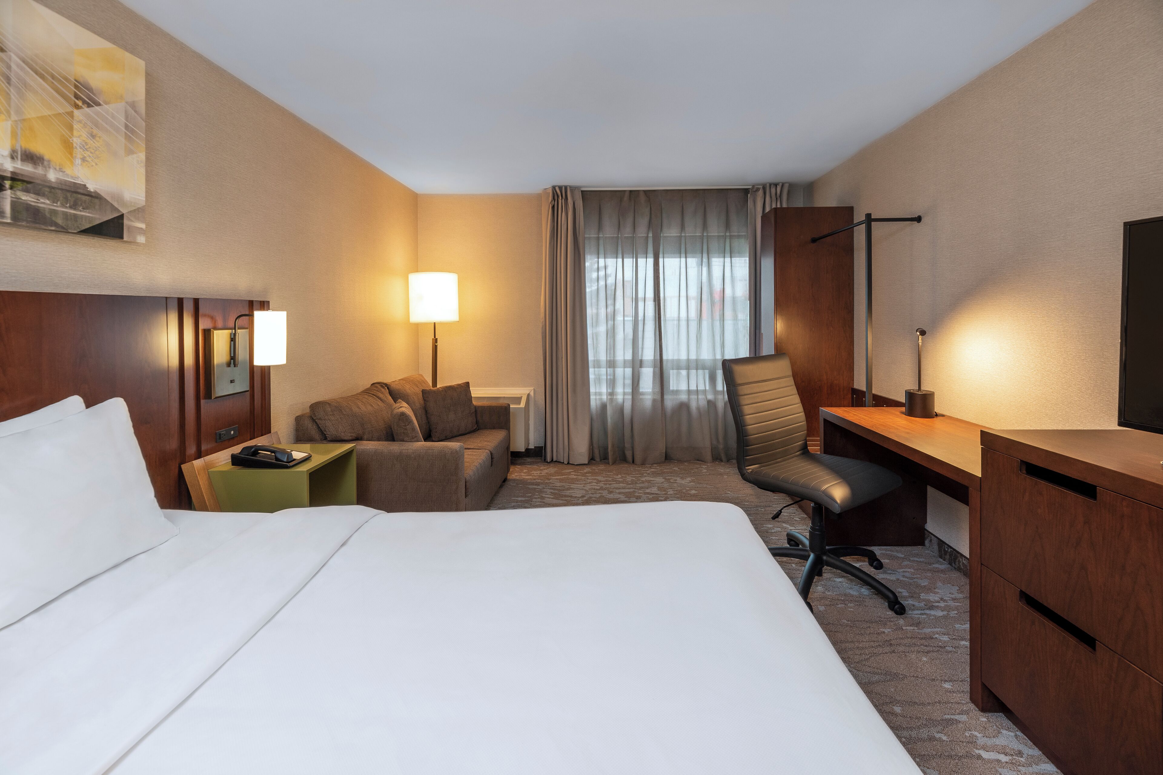 A hotel room with a large bed, a desk, a chair, a small table, and a TV.