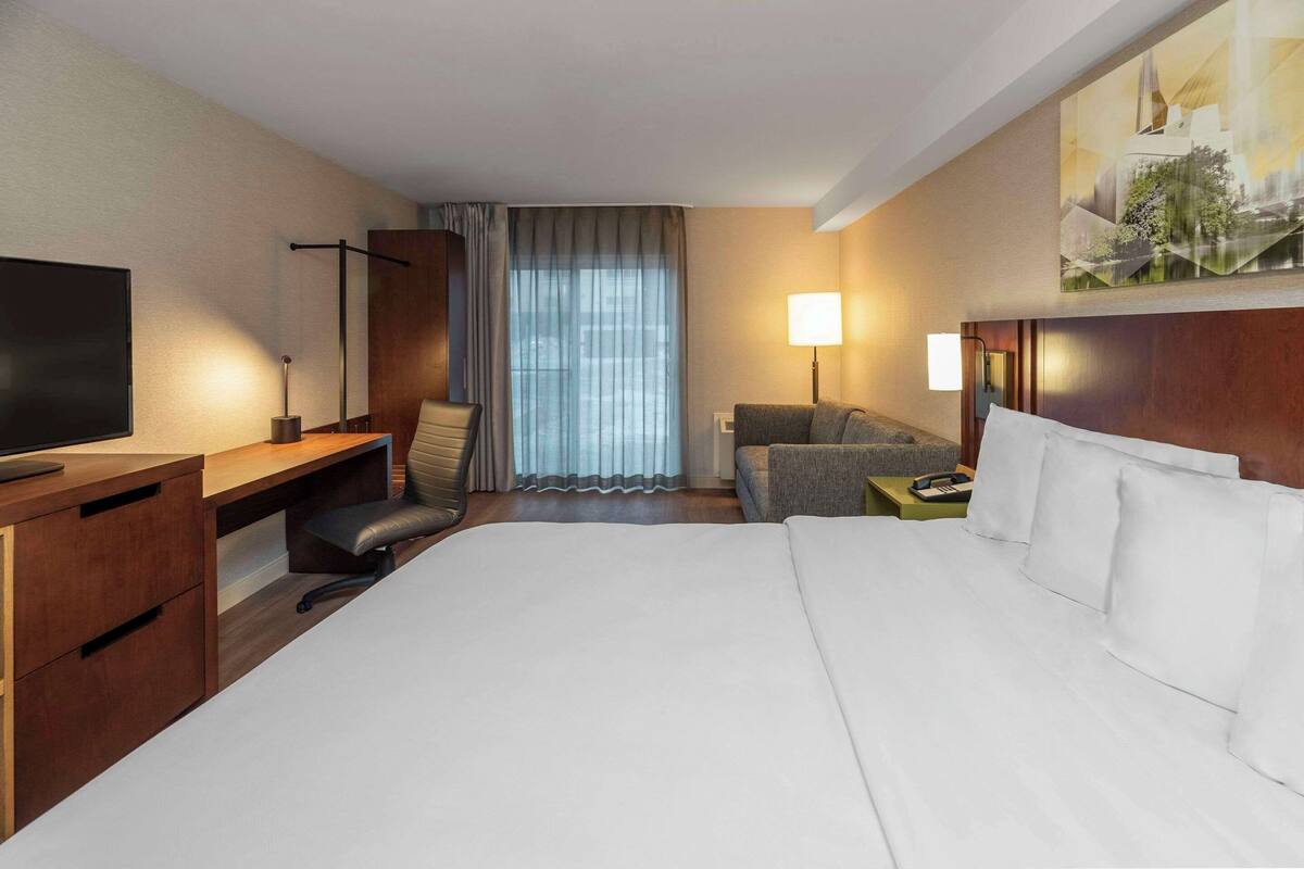 A hotel room with a large bed, a desk, a chair, a TV, a lamp, and a window with curtains.