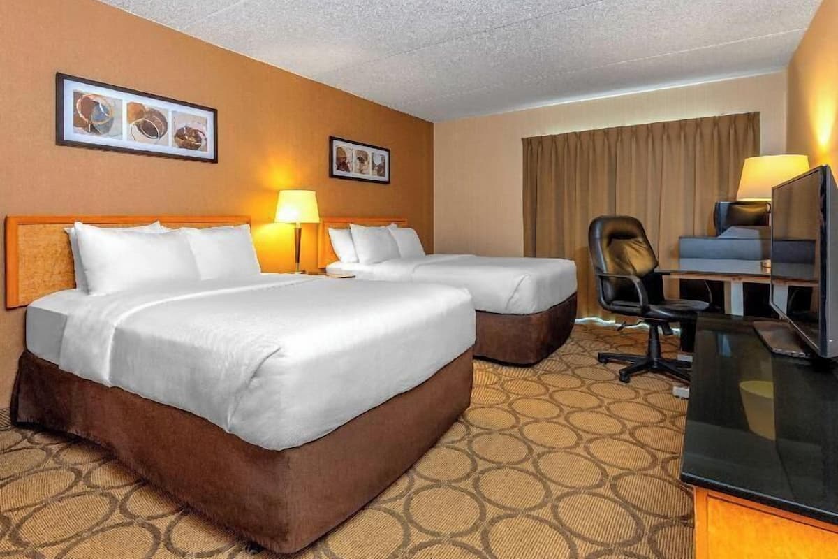 A hotel room with two beds, a desk, a chair, and two lamps.