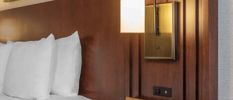 A hotel room with a wooden headboard, a white sofa, a green side table, and a wall-mounted light fixture.