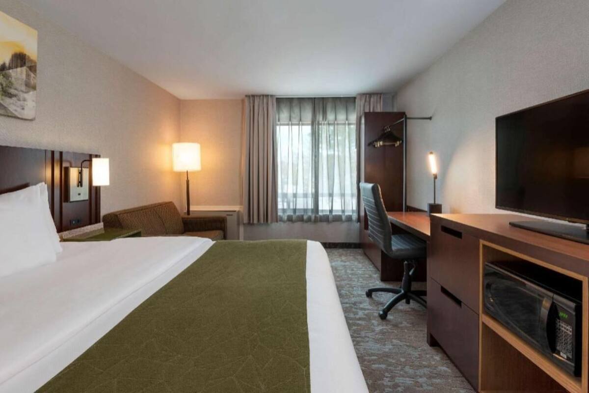 A hotel room with a bed, desk, chair, television, and a window with curtains.