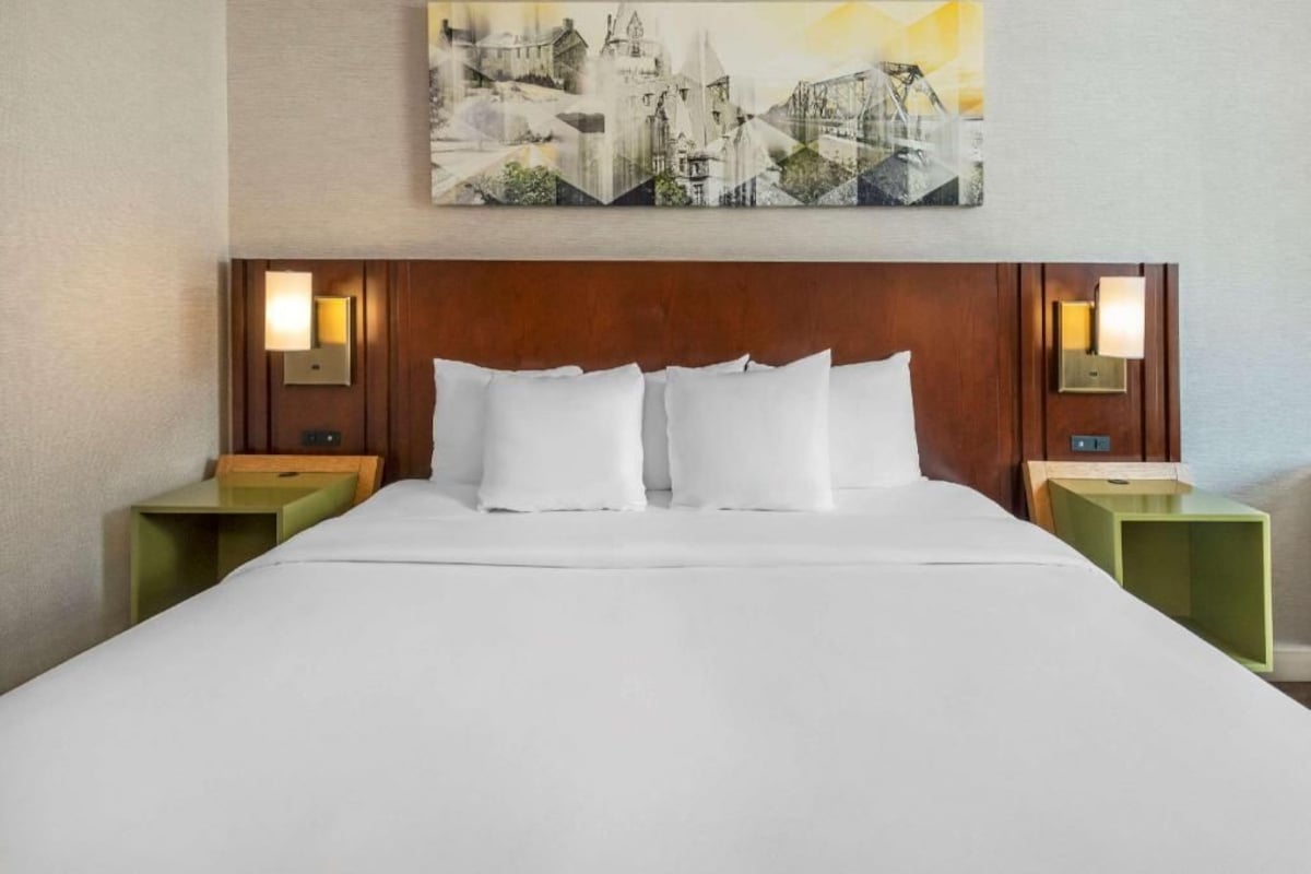A hotel room with a large bed, two bedside tables, and a wall-mounted painting.