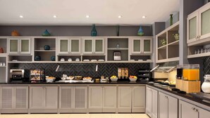 Una cocina moderna con armarios blancos, salpicadero negro y diversos electrodomésticos.