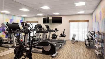A gym with exercise equipment, a mirror, and a wall with a colorful mural.