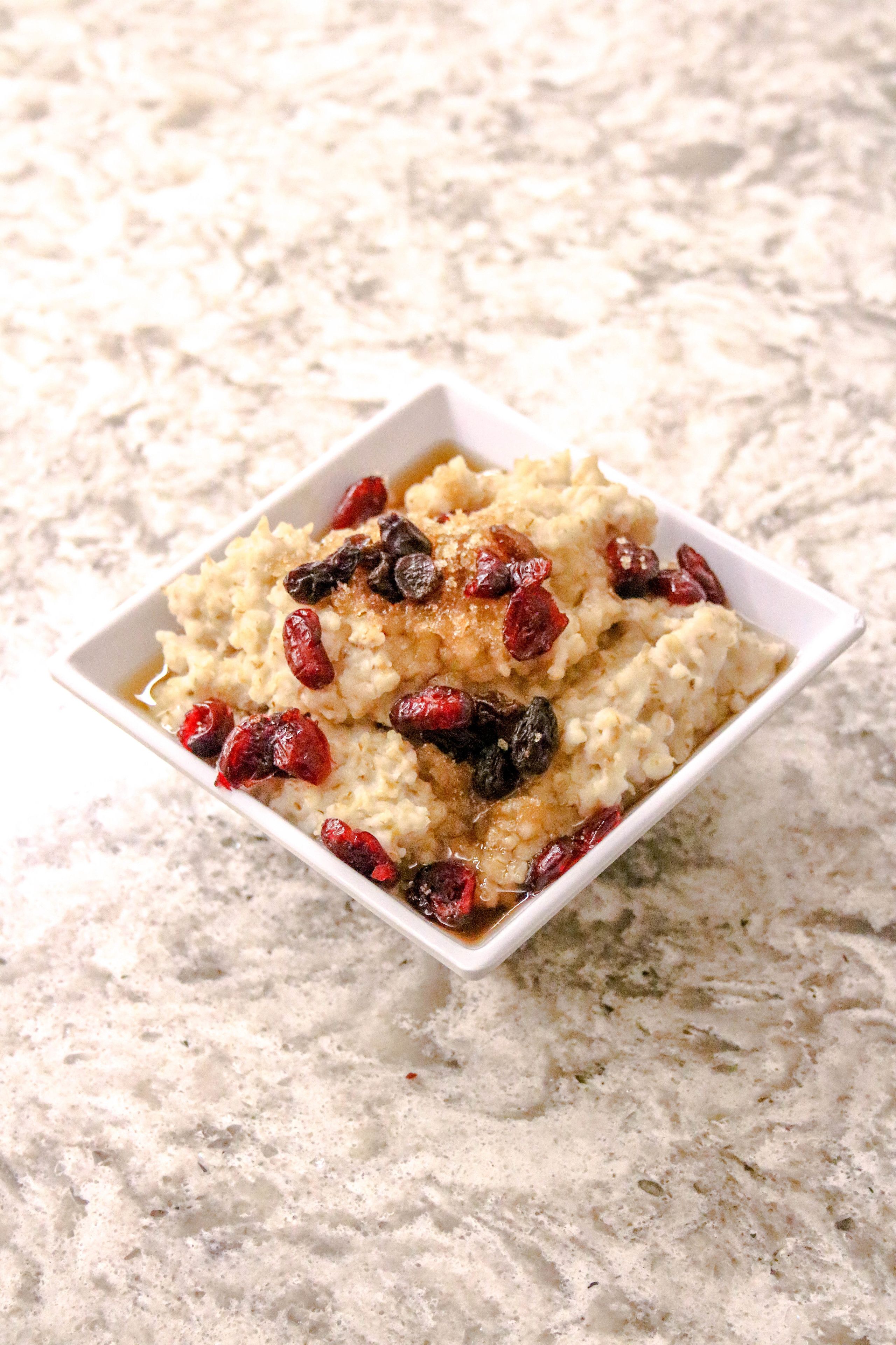 A bowl of oatmeal with raisins and syrup on a textured surface.