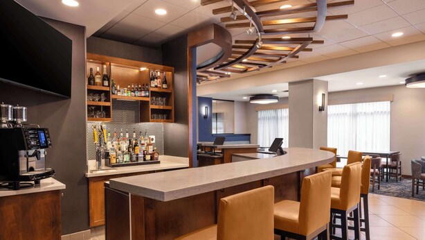 Una zona de bar con una barra alargada, varios taburetes y una selección de botellas y vasos en estanterías.