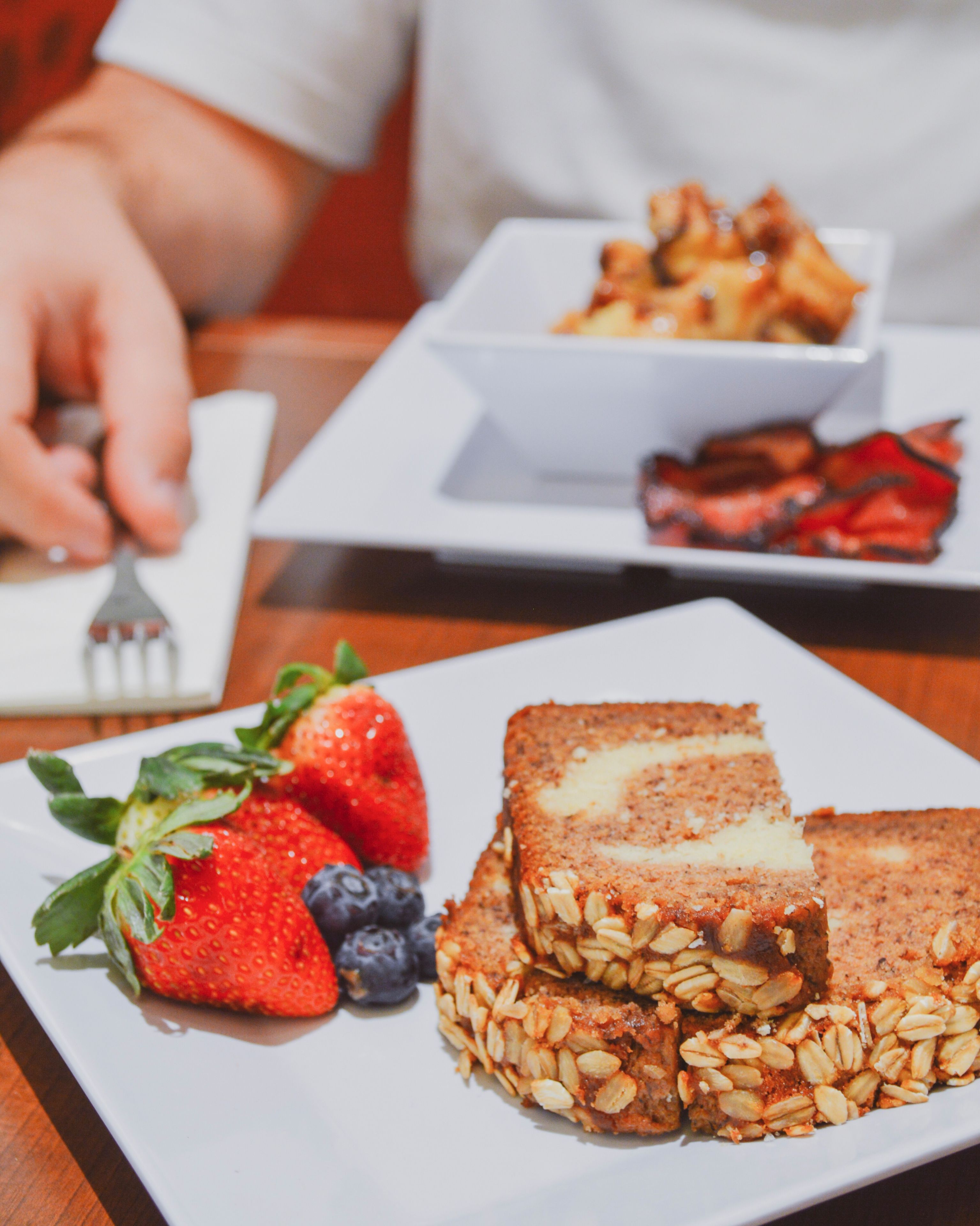 Un plato con una porción de pastel cubierto de avena y una guarnición de fresas y arándanos.