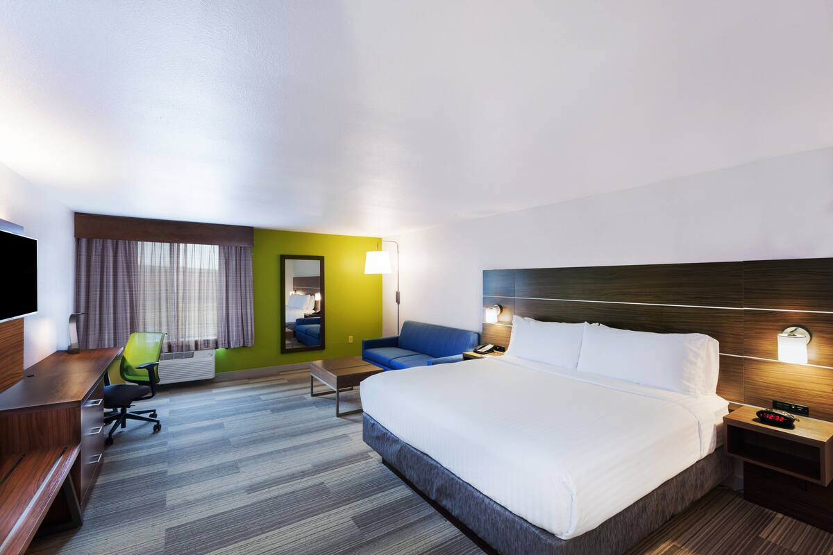 Una habitación de hotel con una cama grande, un escritorio con silla, una mesita, un sofá y un televisor.