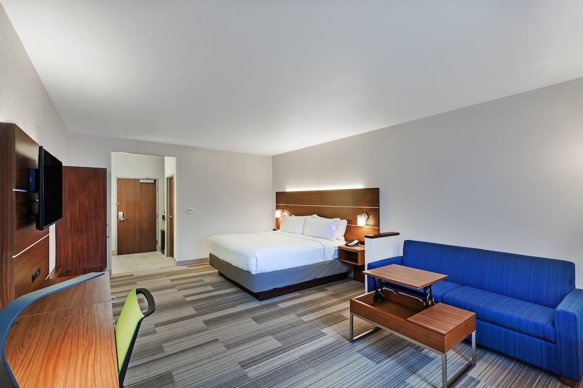 Una habitación de hotel con una cama, un sofá azul, un escritorio, un televisor y un armario de madera.