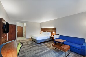 A hotel room with a bed, a blue sofa, a desk, a TV, and a wooden wardrobe. - Holiday Inn Express Hotel & Suites Dallas Lewisville by IHG (Lewisville)