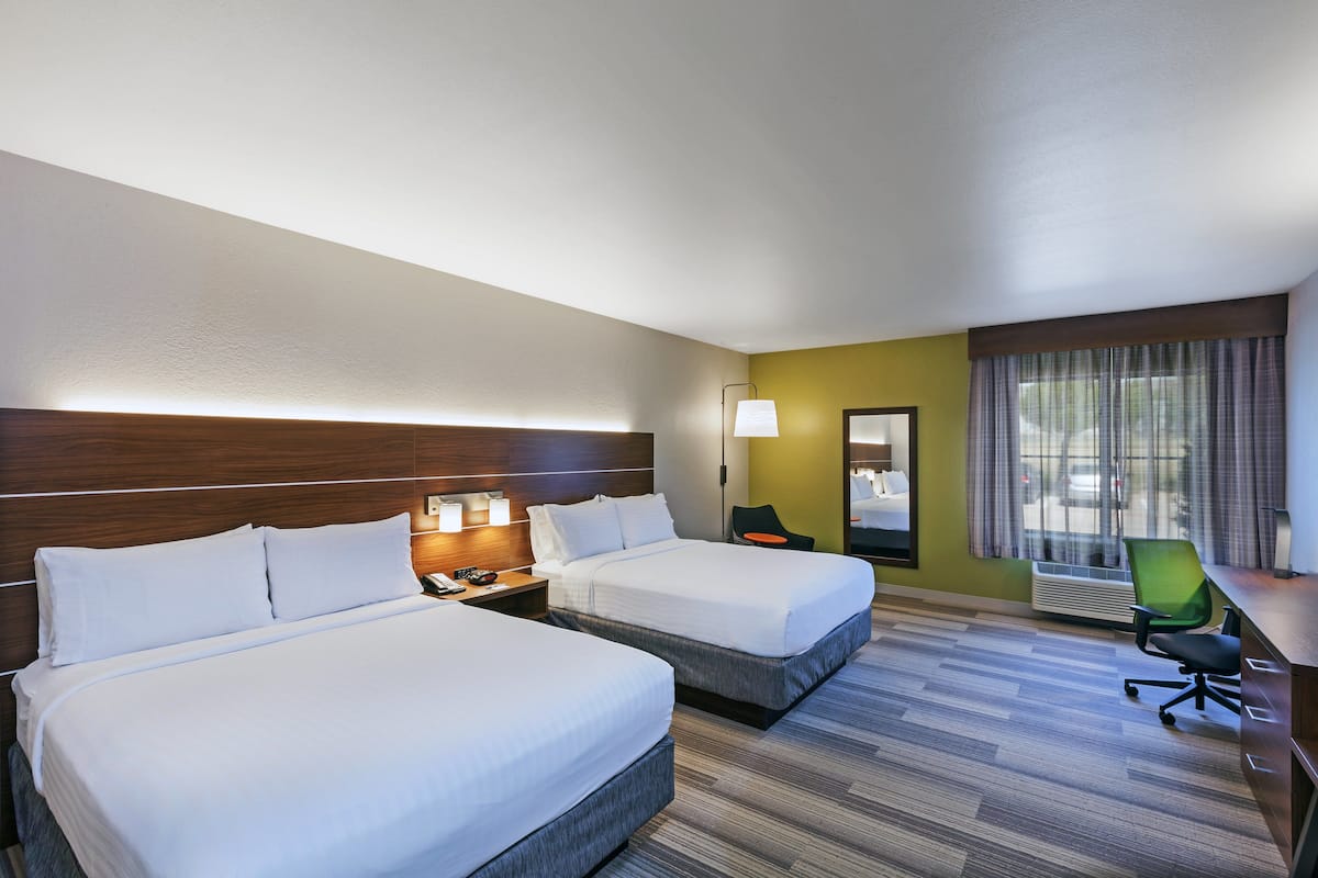 Habitación de hotel con dos camas, un escritorio, una silla y una ventana con cortinas.