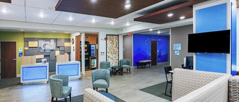 A hotel lobby with seating areas, a reception desk, and a wall-mounted TV.