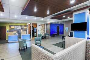 A hotel lobby with seating areas, a reception desk, and a wall-mounted TV.