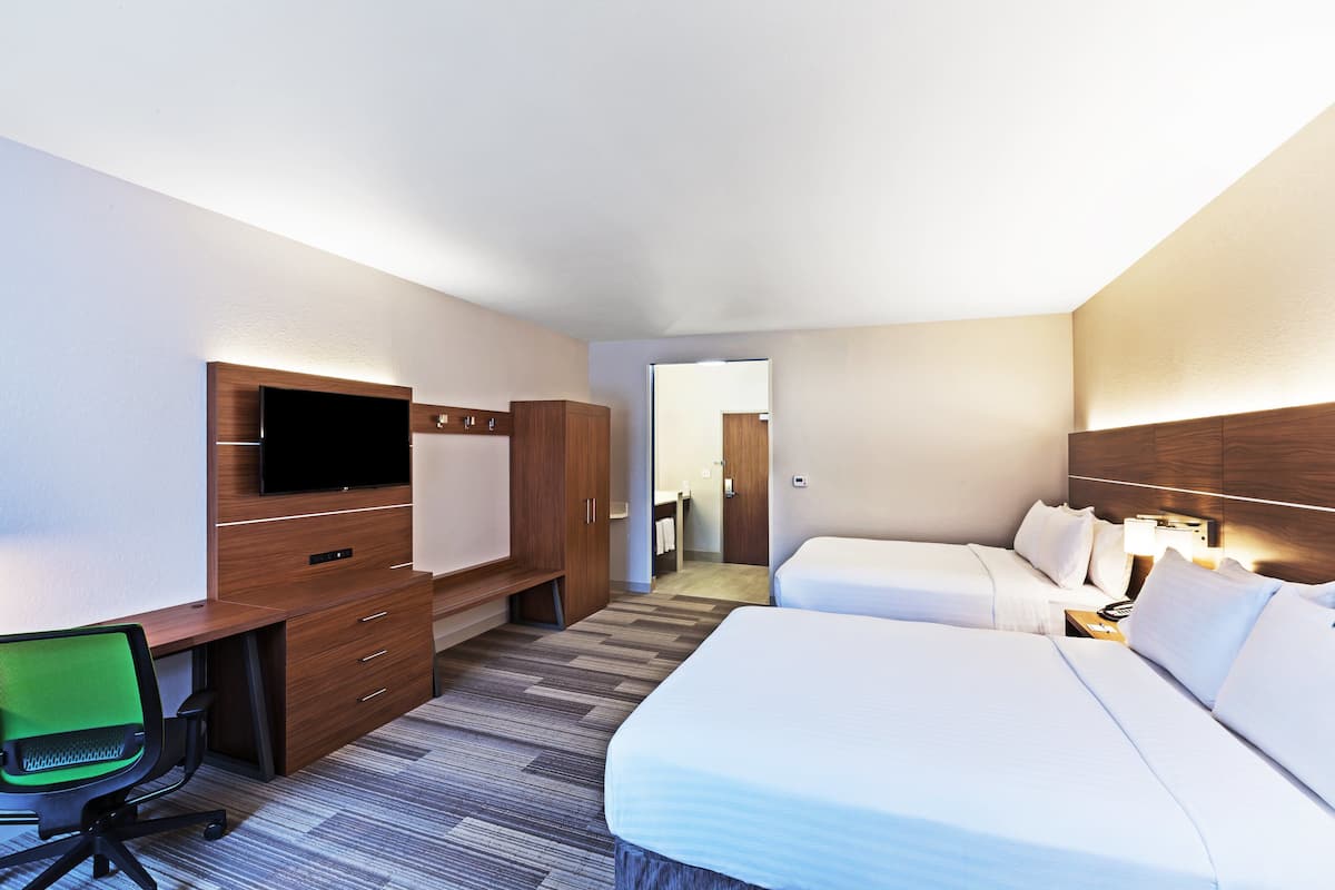 Habitación de hotel con escritorio, televisor, dos camas y un baño visible a través de una puerta abierta.