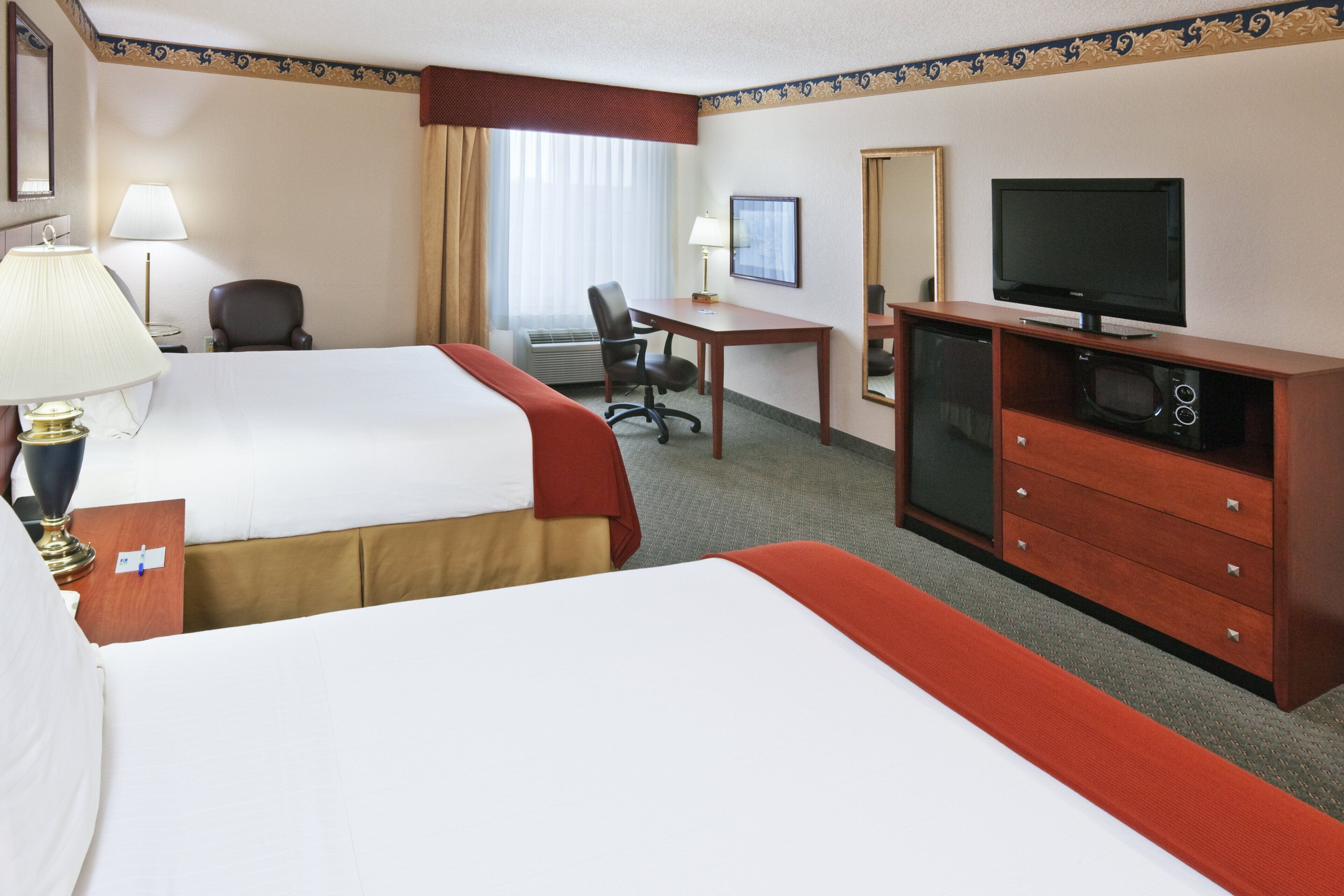 A hotel room with two beds, a desk, a chair, a television, and a minibar.
