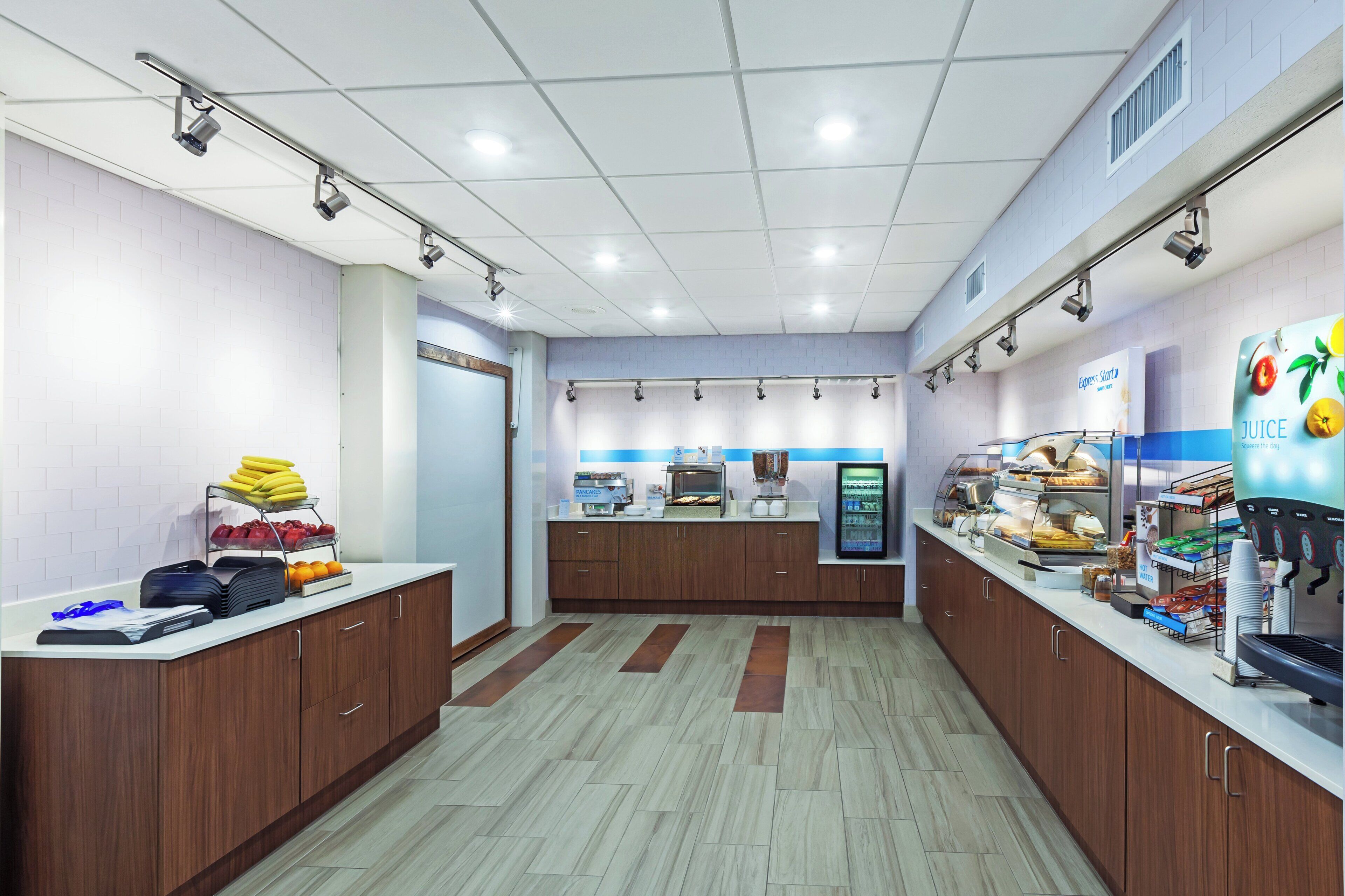 Un espace moderne dédié au petit-déjeuner, doté d’un buffet où les clients peuvent se servir eux-mêmes, d’un distributeur de jus et d’un écran numérique affichant le menu.
