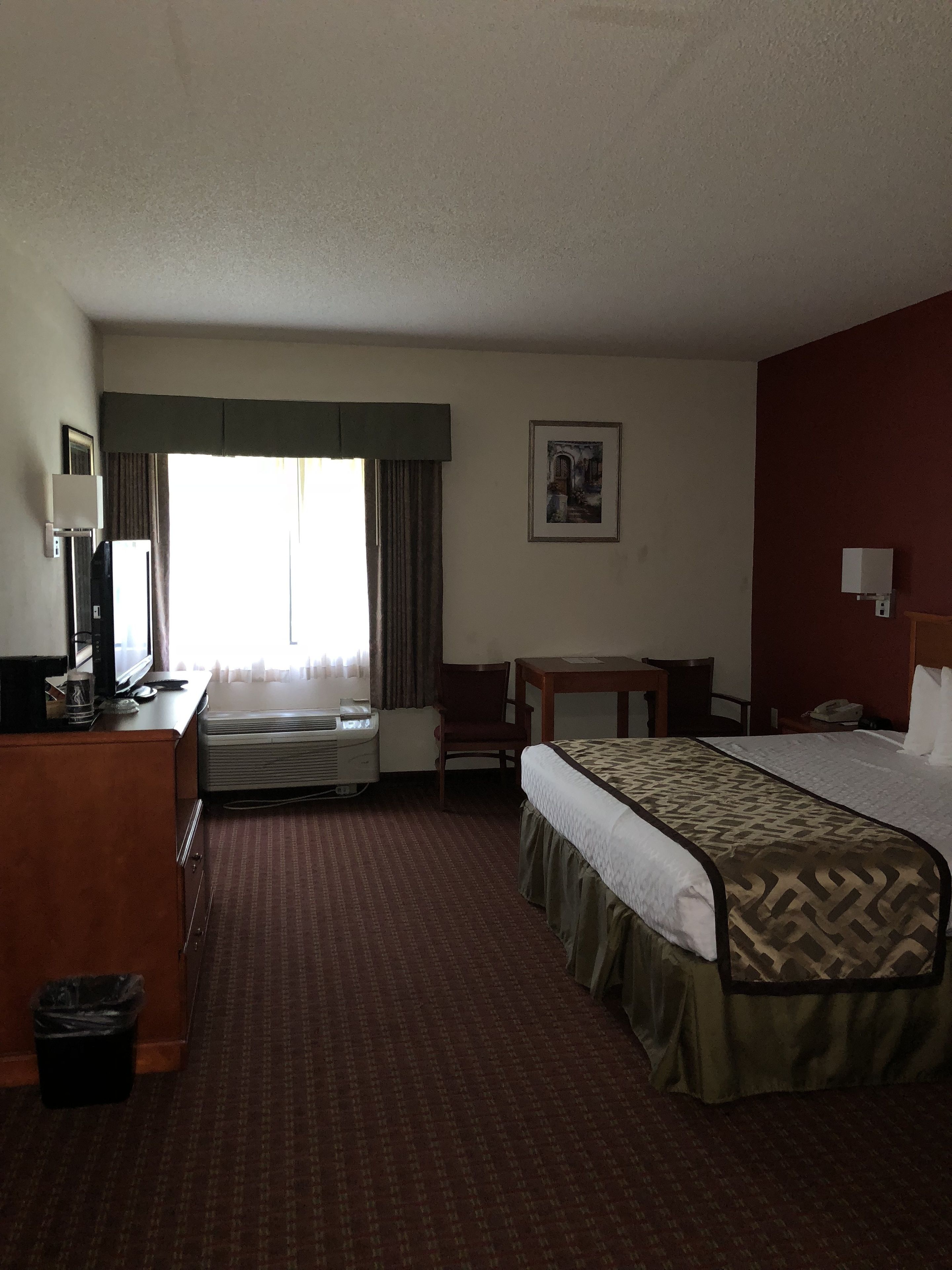 Una habitación de hotel con cama, escritorio, silla y ventana con cortinas.