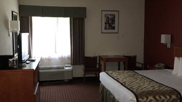 Una habitación de hotel con cama, escritorio, silla y ventana con cortinas.