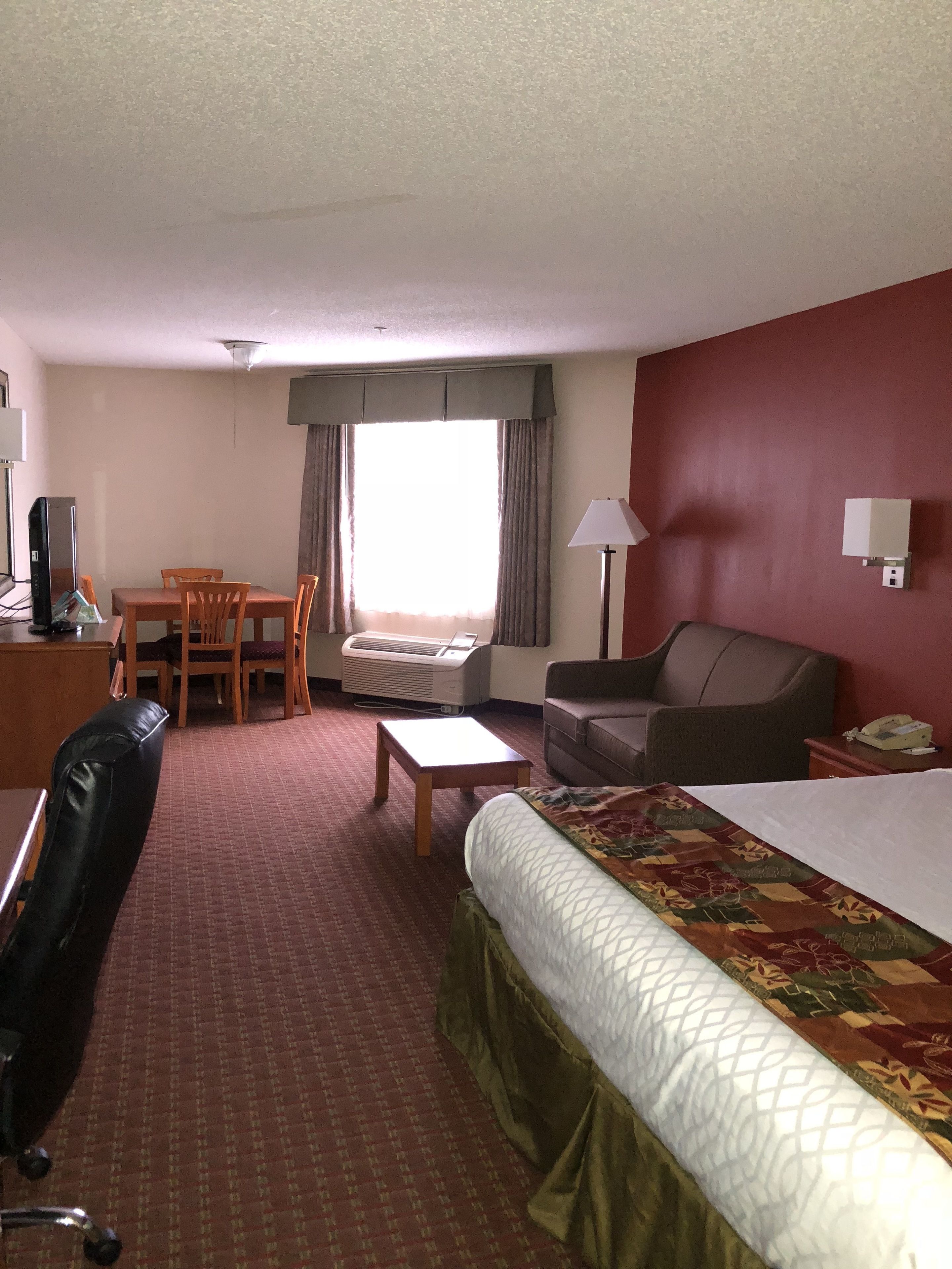 A hotel room with a bed, a desk with a computer, a chair, a sofa, a lamp, and a window with curtains.