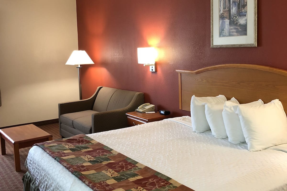 Ein Hotelzimmer mit einem großen Bett, einem Nachttisch, einer Lampe, einem Sessel und einem Bild an der Wand.