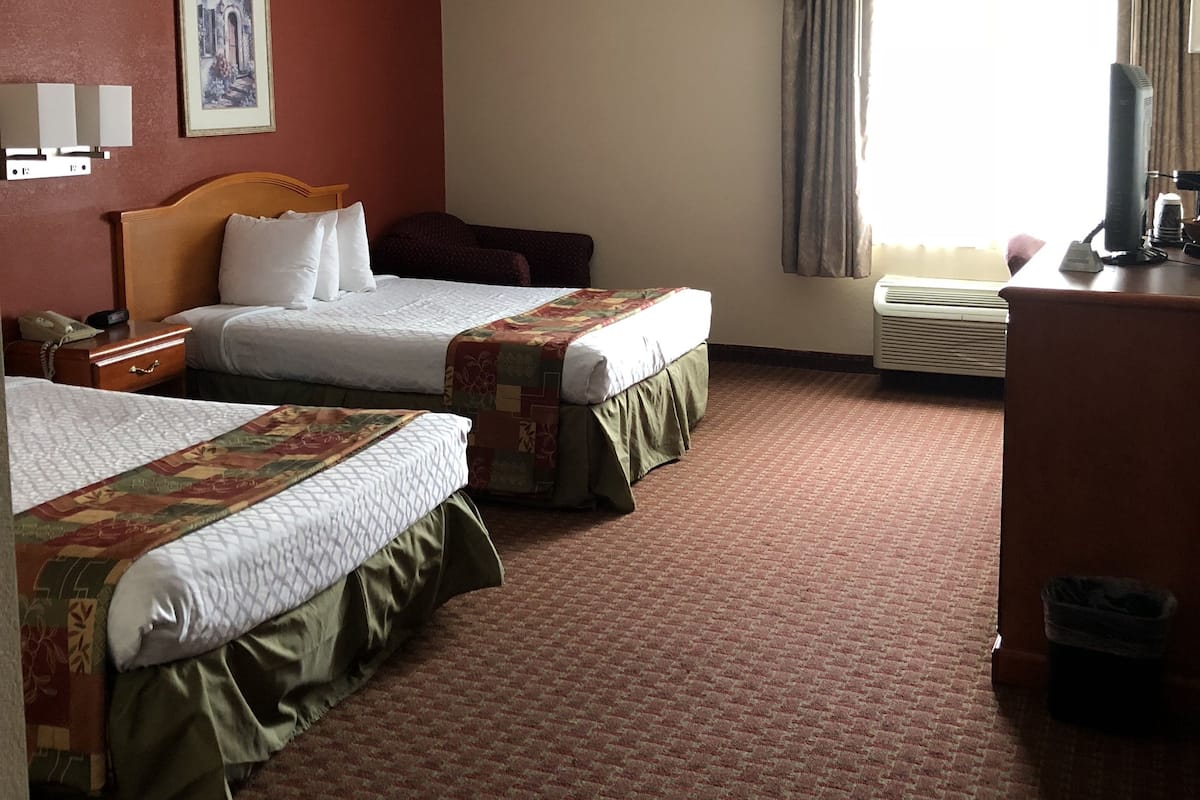 Ein Hotelzimmer mit zwei Betten, einem Schreibtisch, einem Stuhl, einem Fernseher und einem Fenster mit Vorhängen.