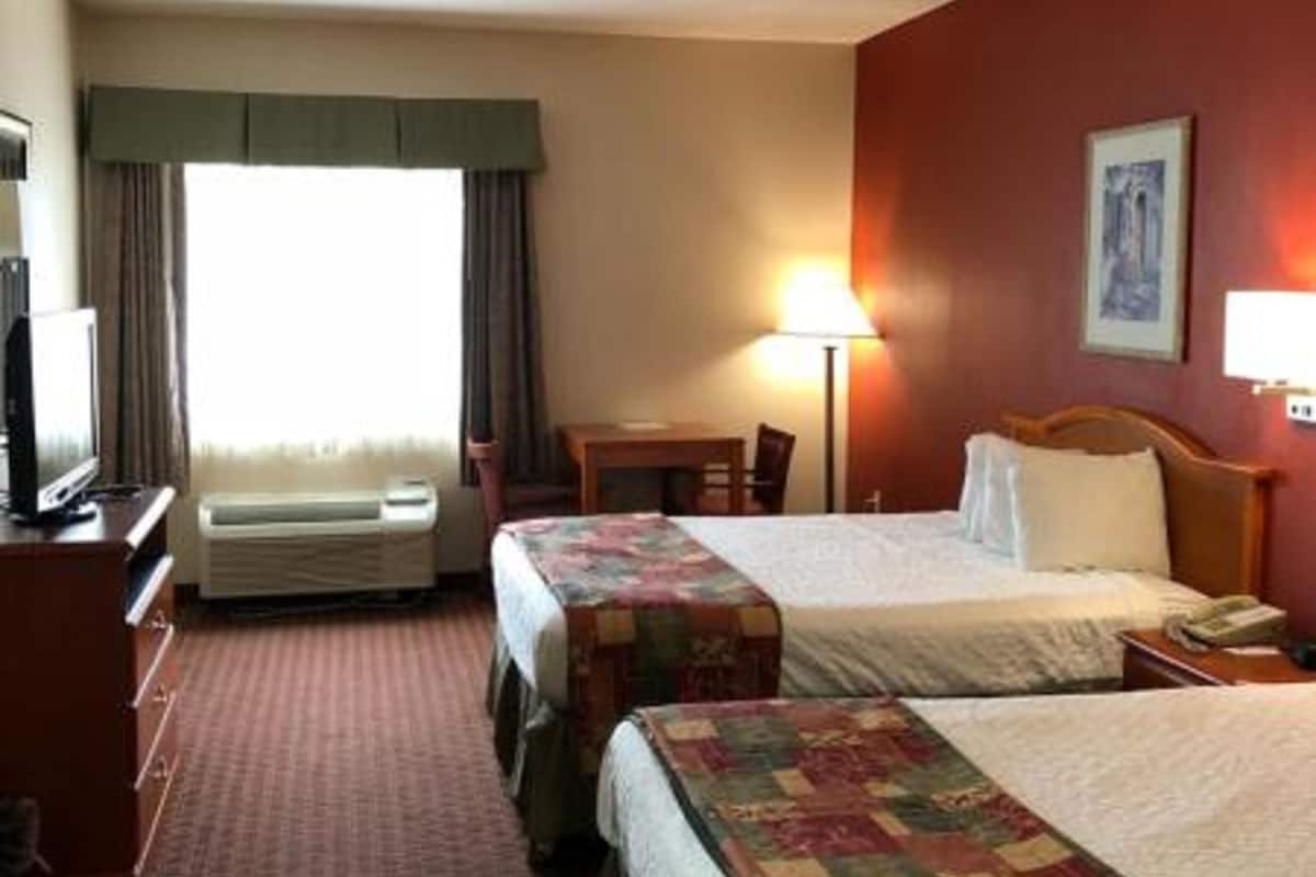 Ein Hotelzimmer mit zwei Betten, einem Schreibtisch, einem Stuhl, einem Fernseher und einem fenster mit Vorhängen.
