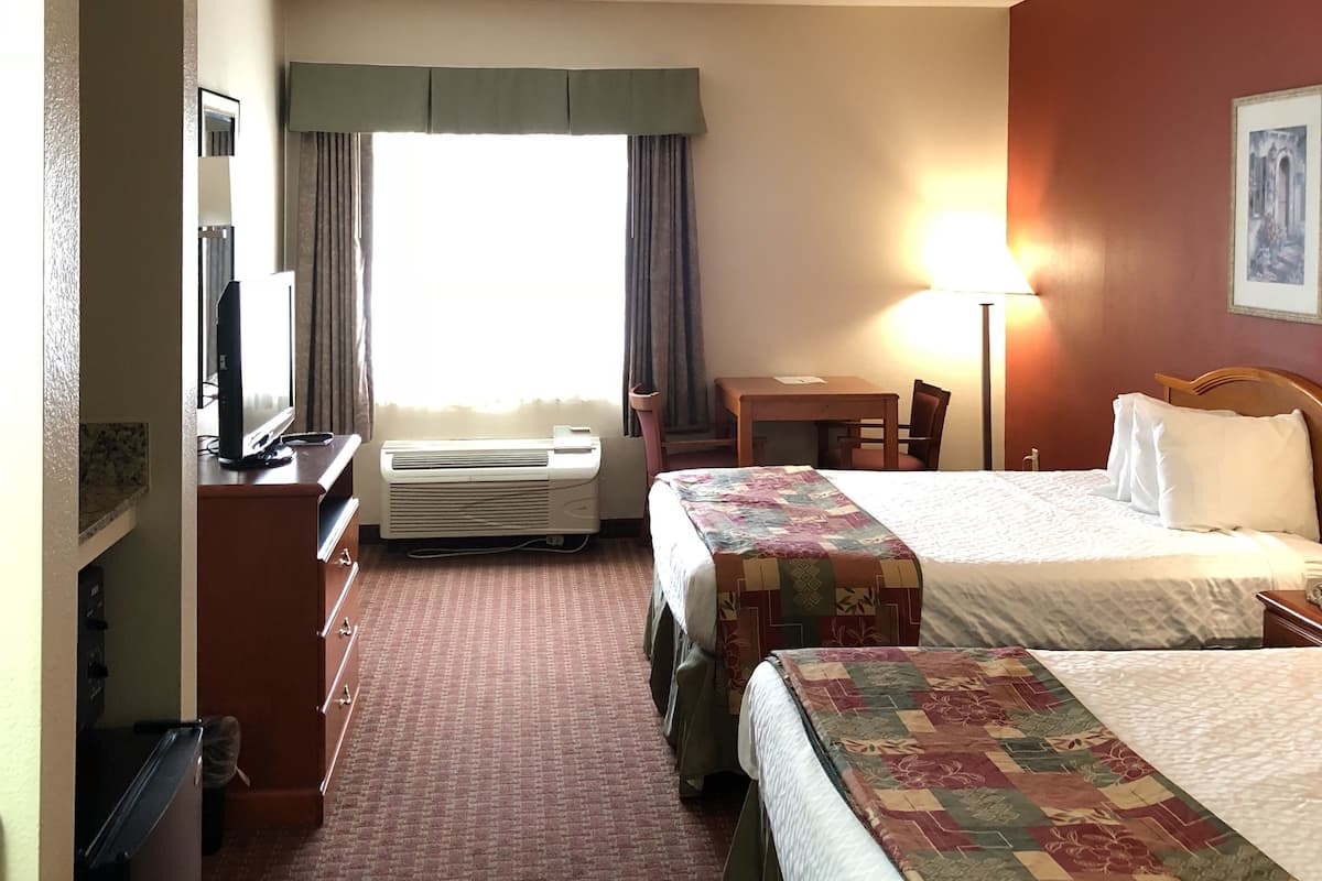 Ein Hotelzimmer mit zwei Betten, einem Schreibtisch, einem Sessel, einem Fernseher und einem Fenster mit Vorhängen.
