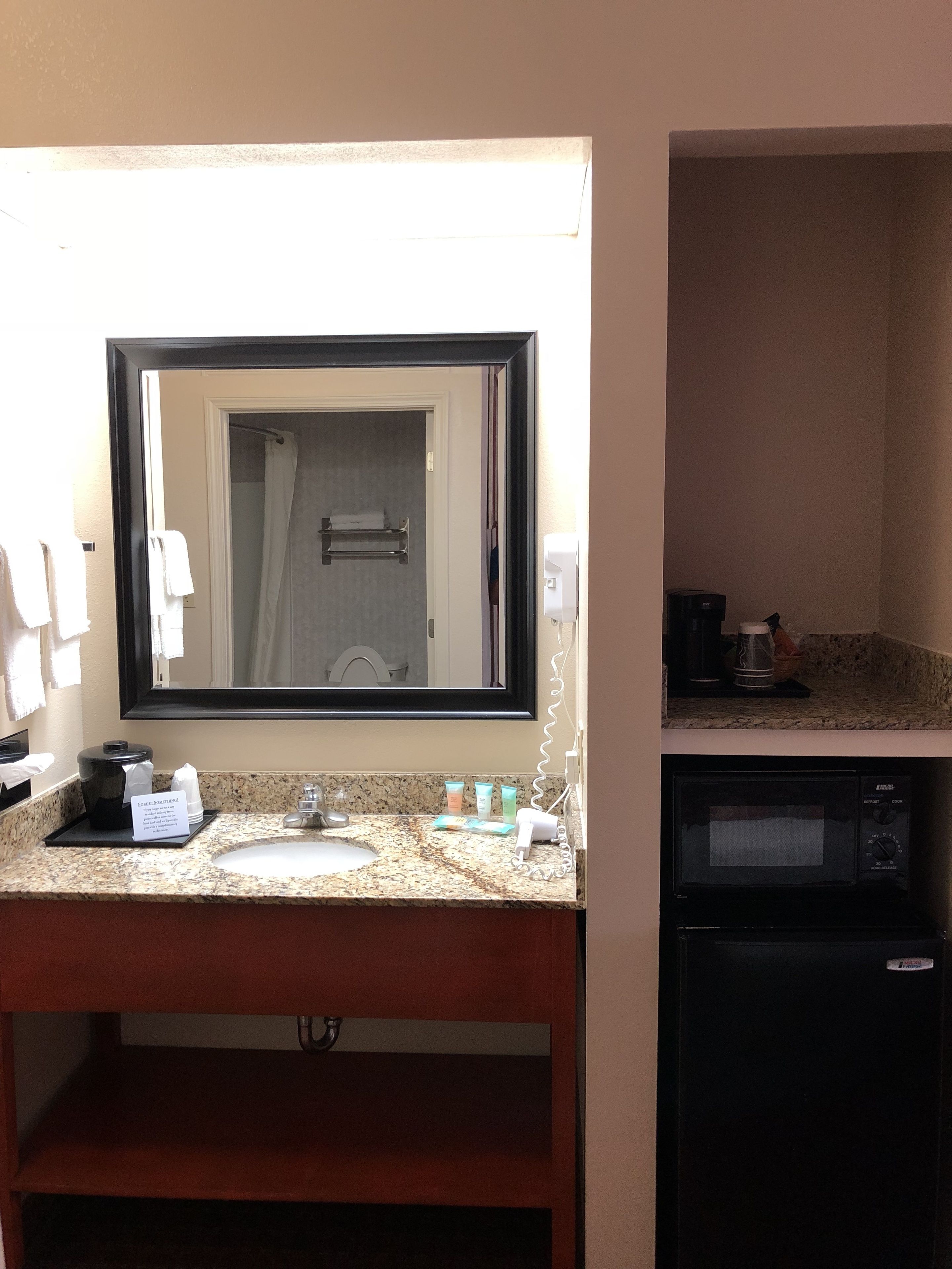 A bathroom with a sink, mirror, and a coffee maker.