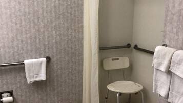 A shower area with a white shower curtain, a grab bar, a white chair, and a towel rack with towels.