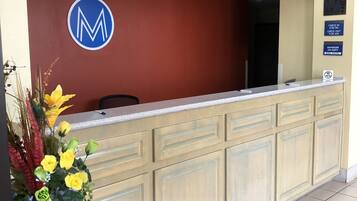 A reception desk with a logo, a check-in/out sign, and a 'No Pets' sign.